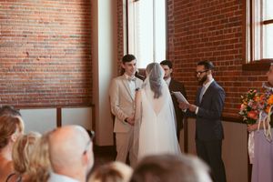 A wedding ceremony taking place in a rustic brick-walled venue with guests watching the couple exchange vows.