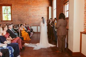 Wedding ceremony in a rustic brick venue with guests seated on wooden chairs viewing couple at the altar.