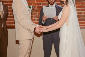 Newlyweds exchange vows during intimate indoor ceremony with exposed brick wall and warm lighting.