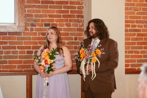 A wedding couple holding colorful autumn bouquets while standing in front of exposed brick walls.