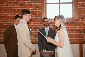 Rustic brick wall wedding venue with natural light streaming through windows serves as backdrop for tender romantic moments.