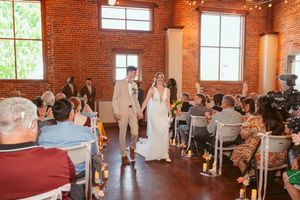 A couple walks down the aisle at a rustic brick venue filled with seated guests during an intimate wedding ceremony.
