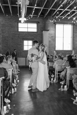A couple shares their first dance at a wedding reception in a rustic brick-walled venue with exposed ductwork.