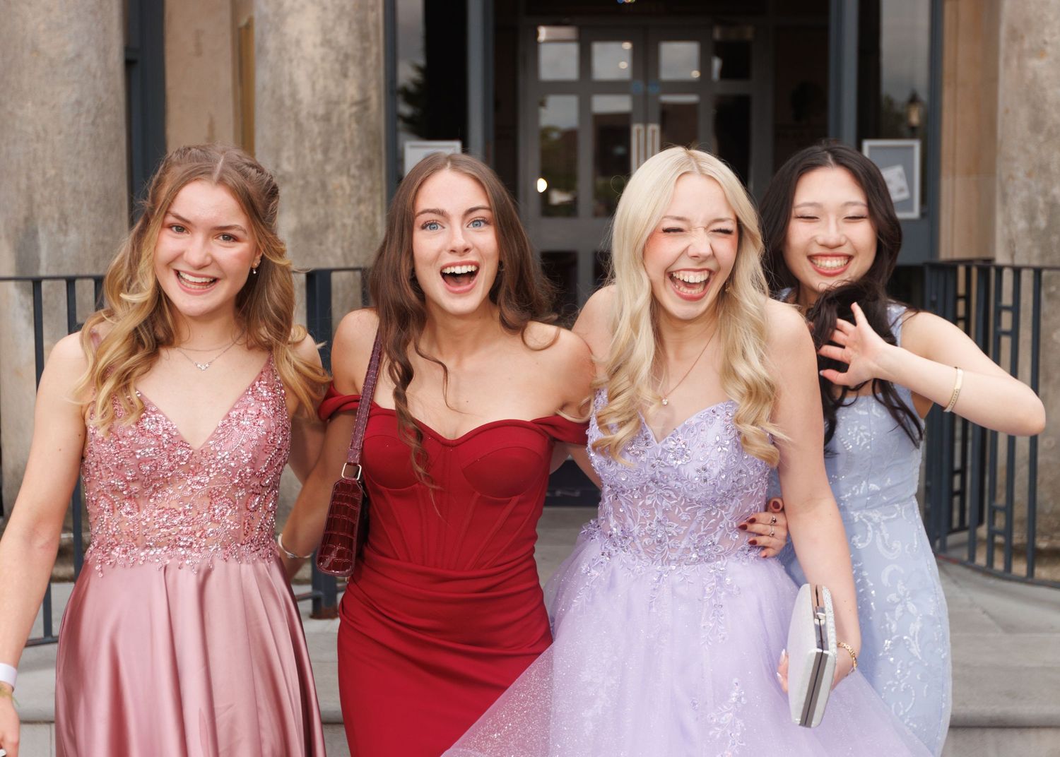 Group of friends in formal dresses posing together at an event with pink and burgundy colored gowns.
