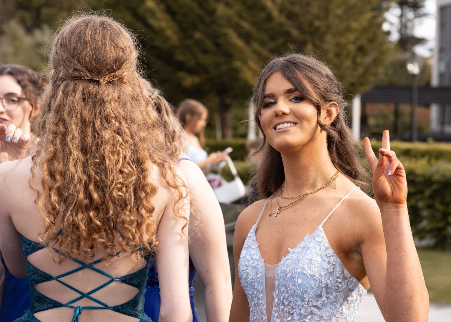 Group of friends in elegant dresses posing and laughing together at an outdoor event.