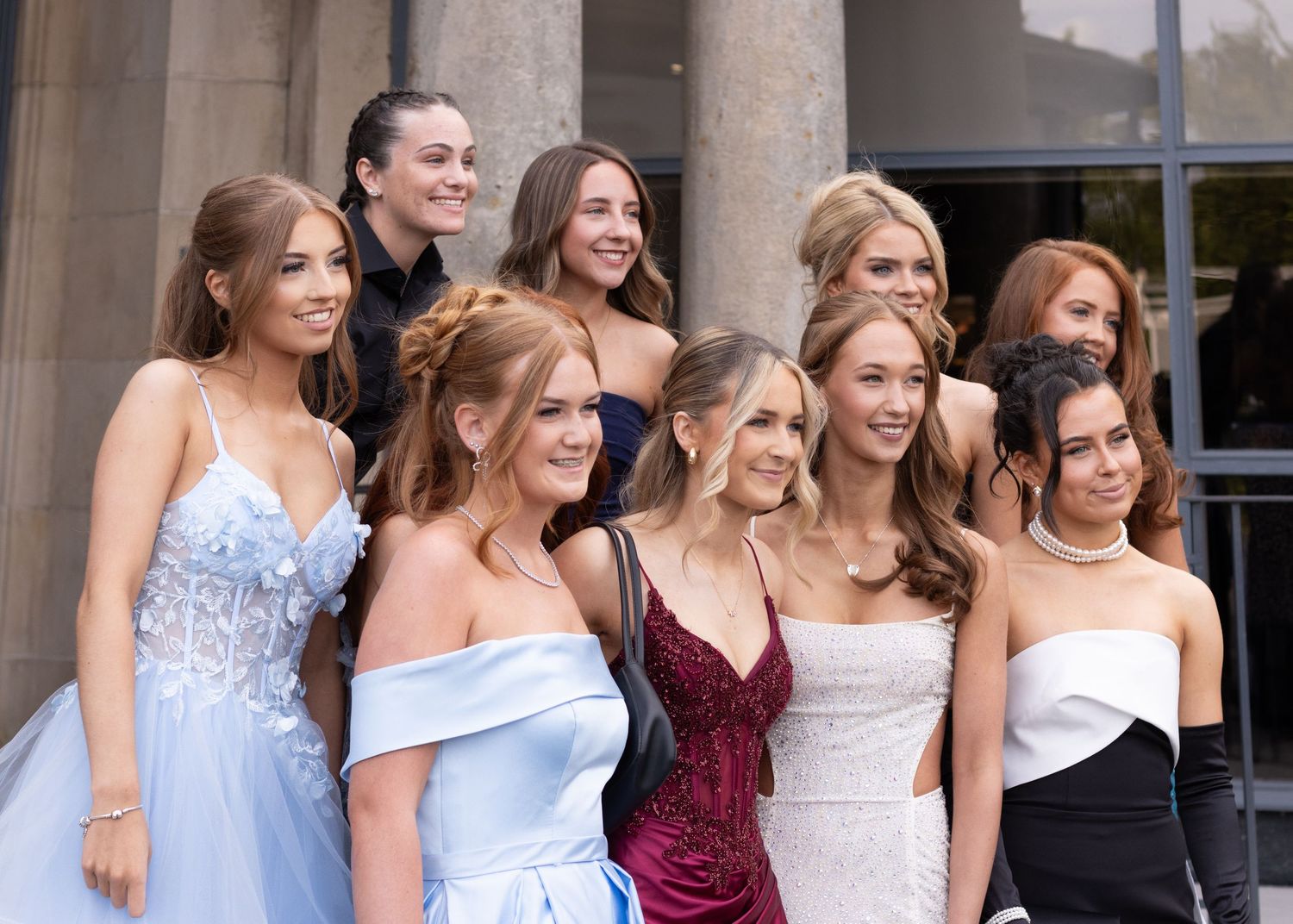 Group of people in formal attire posing together at an elegant venue with columns in background.