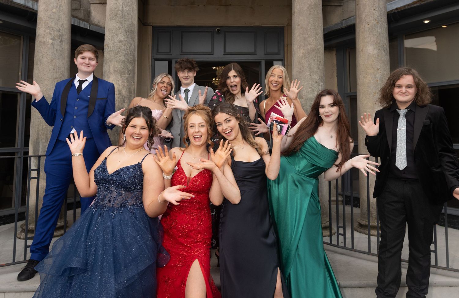 Large group of formal-dressed individuals gathered for a panoramic photo in front of columned building.