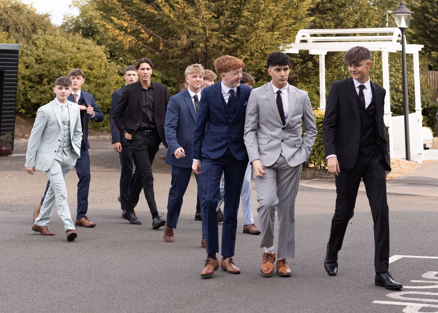 A group of well-dressed individuals walk together outdoors while wearing stylish suits and formal attire.