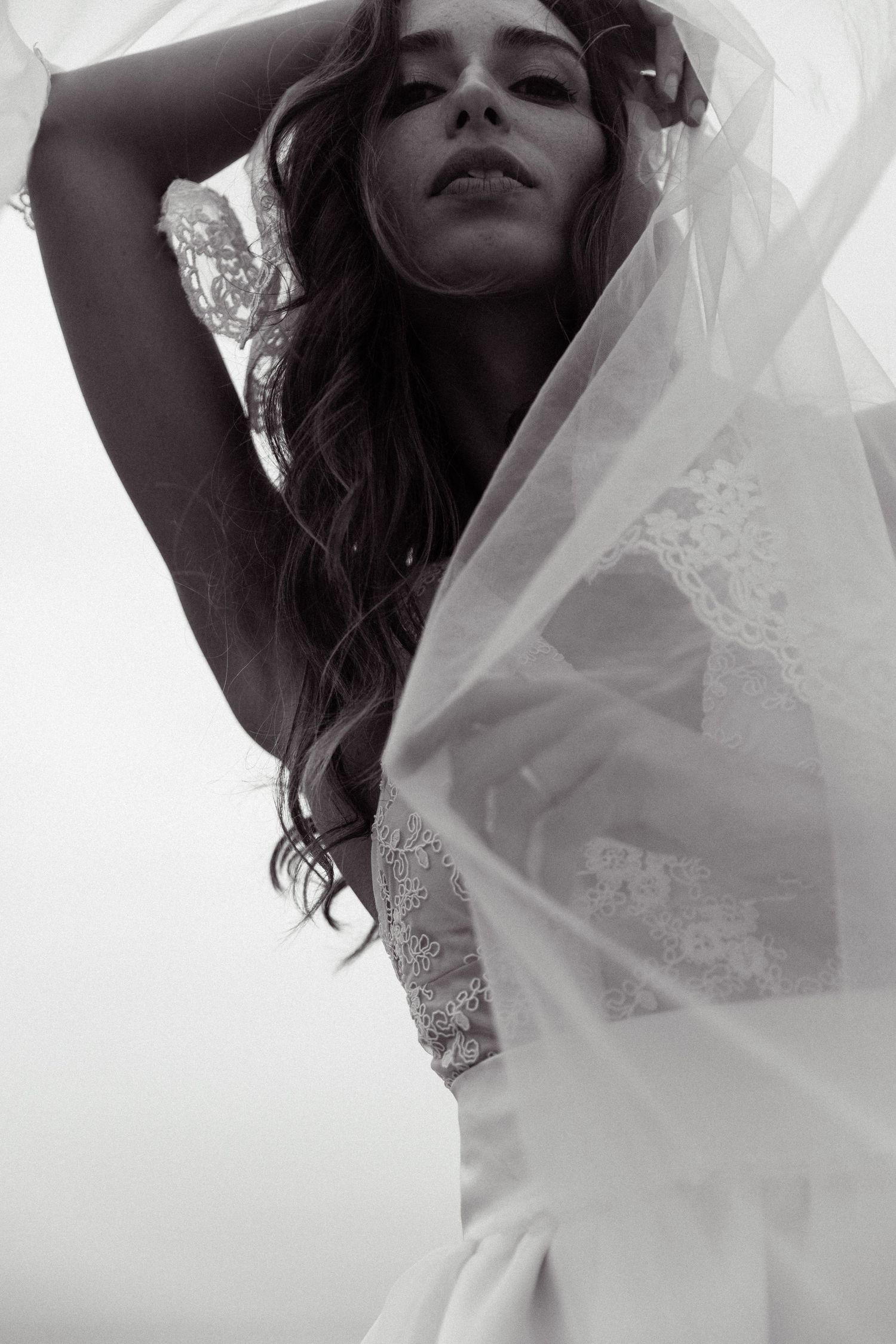 Artistic black and white bridal portrait showing flowing veil and lace wedding dress against light background.