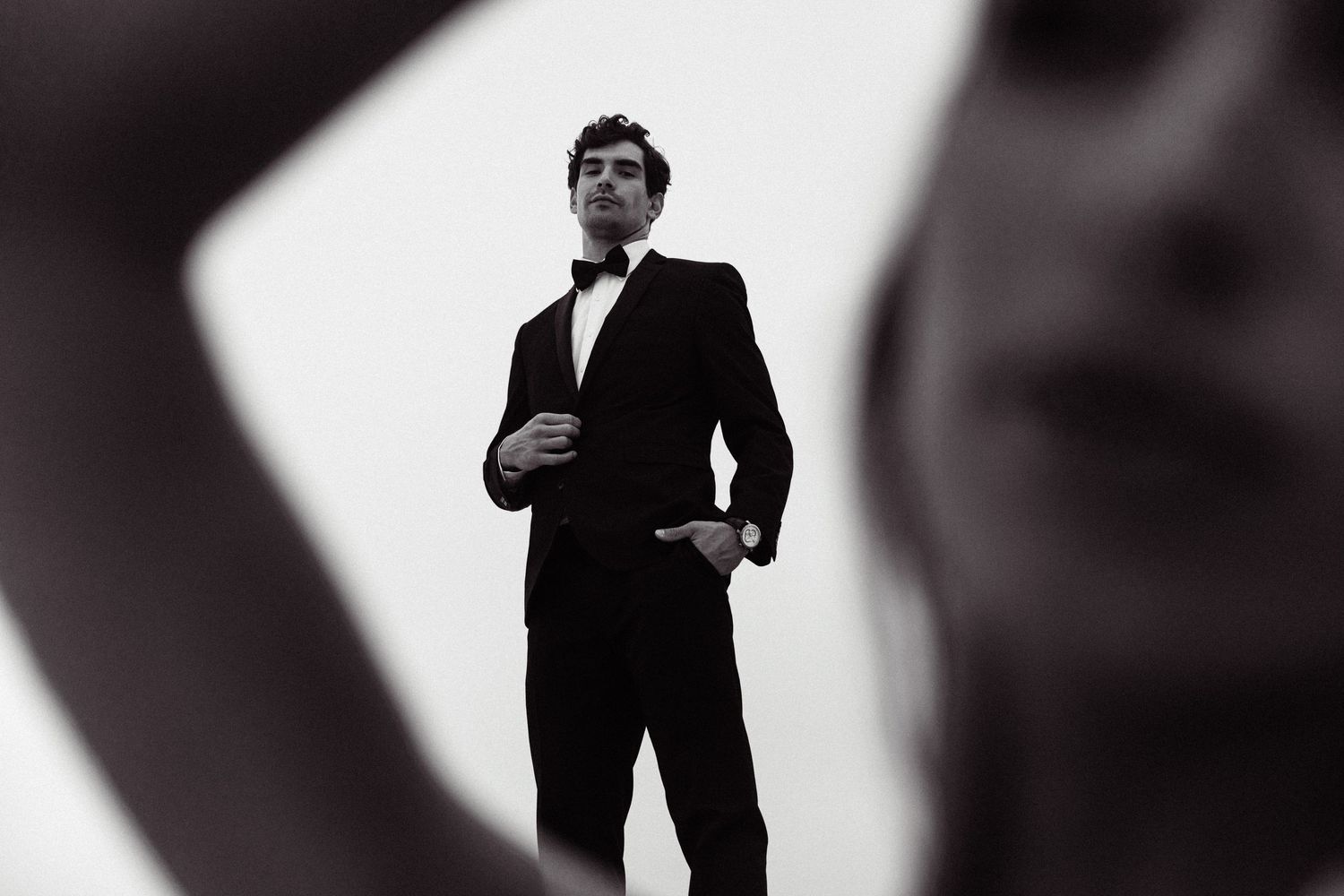 Dramatic black and white portraits of groom in tuxedo against stark background.