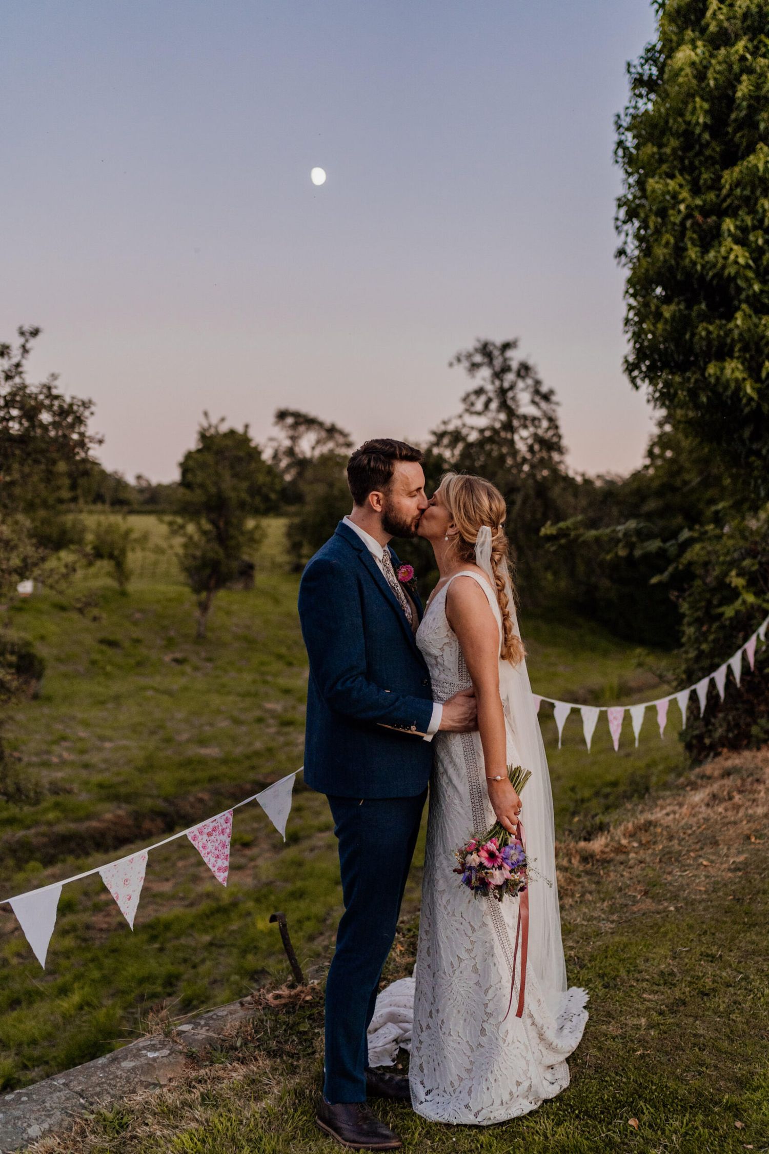 Sunset wedding portraits with white bunting decorations in a rustic outdoor setting.