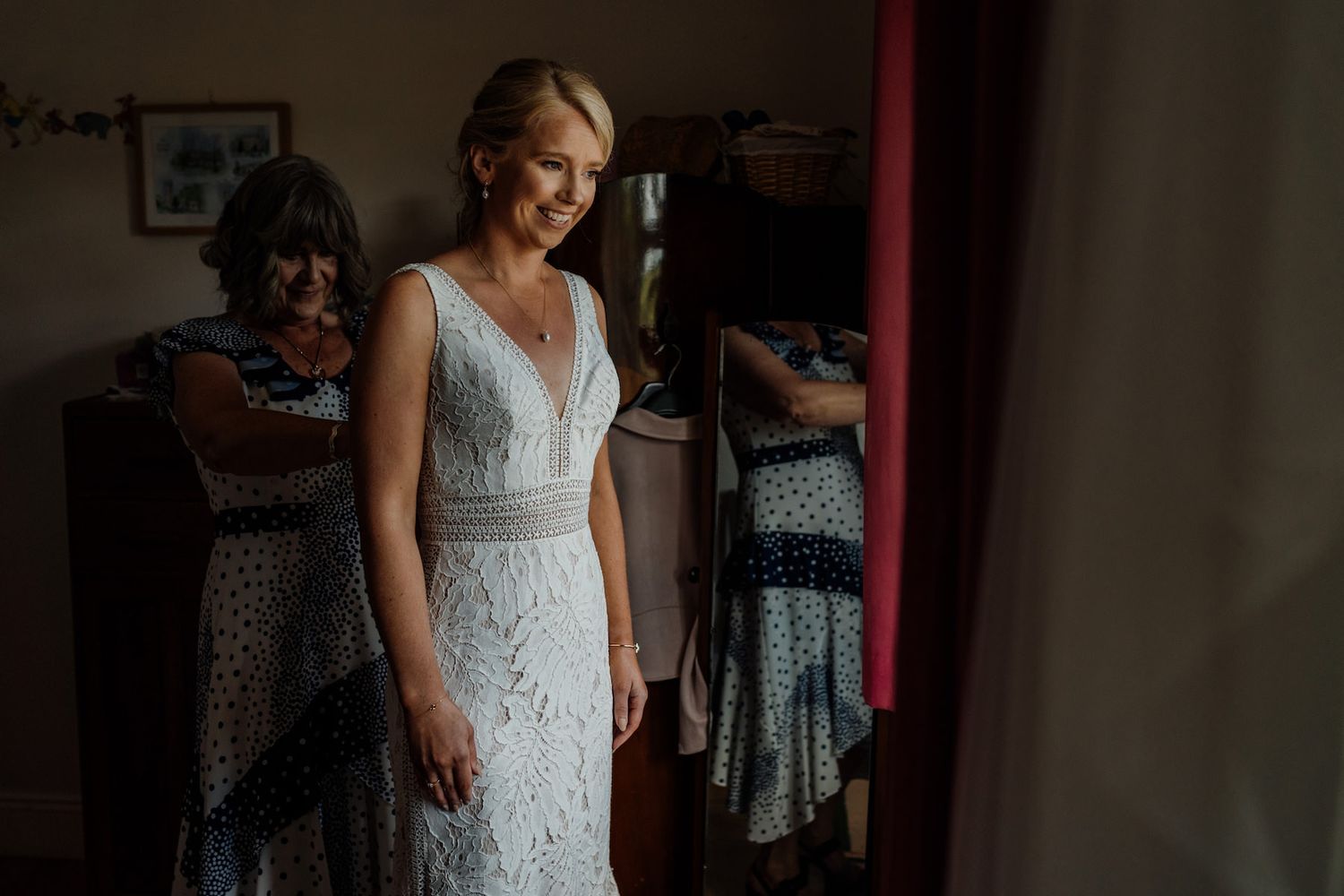Elegant white lace wedding dress details shown in a dimly lit dressing room.