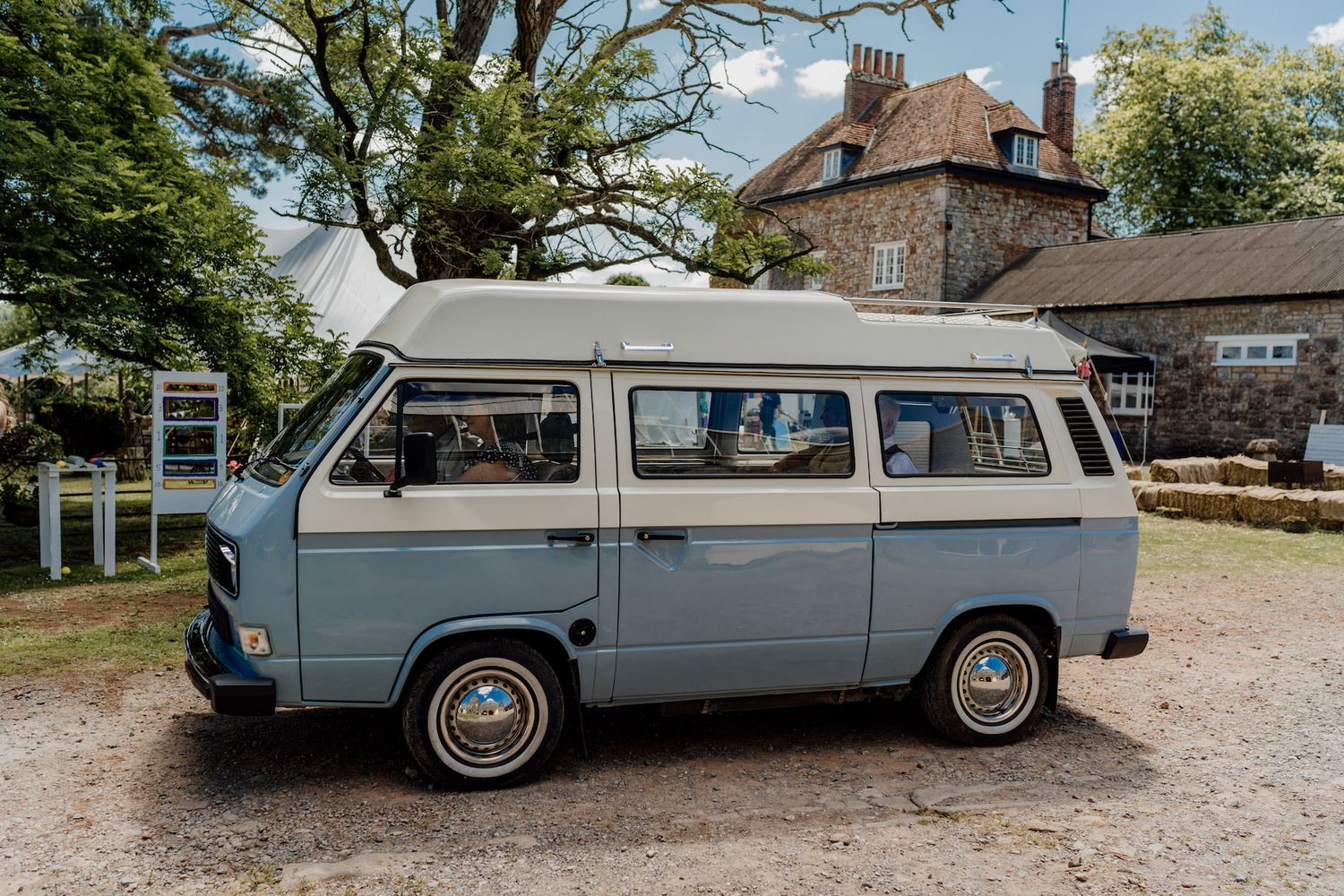 Vintage blue station wagon parked on gravel driveway near rustic buildings.