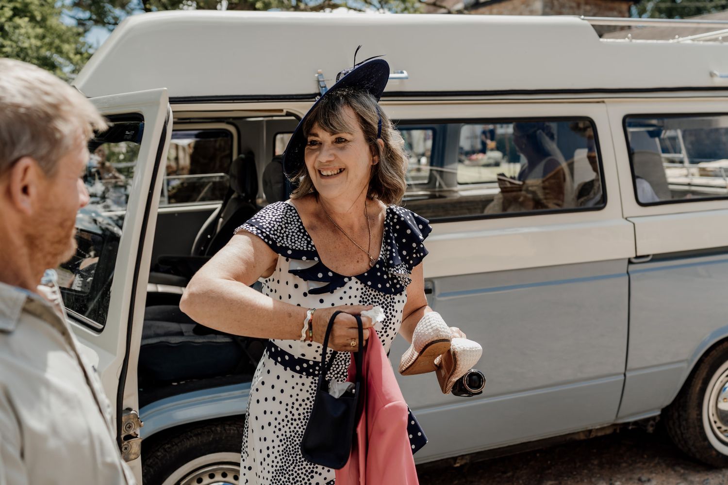 A vintage white van parked outdoors with someone in a polka dot dress disembarking.