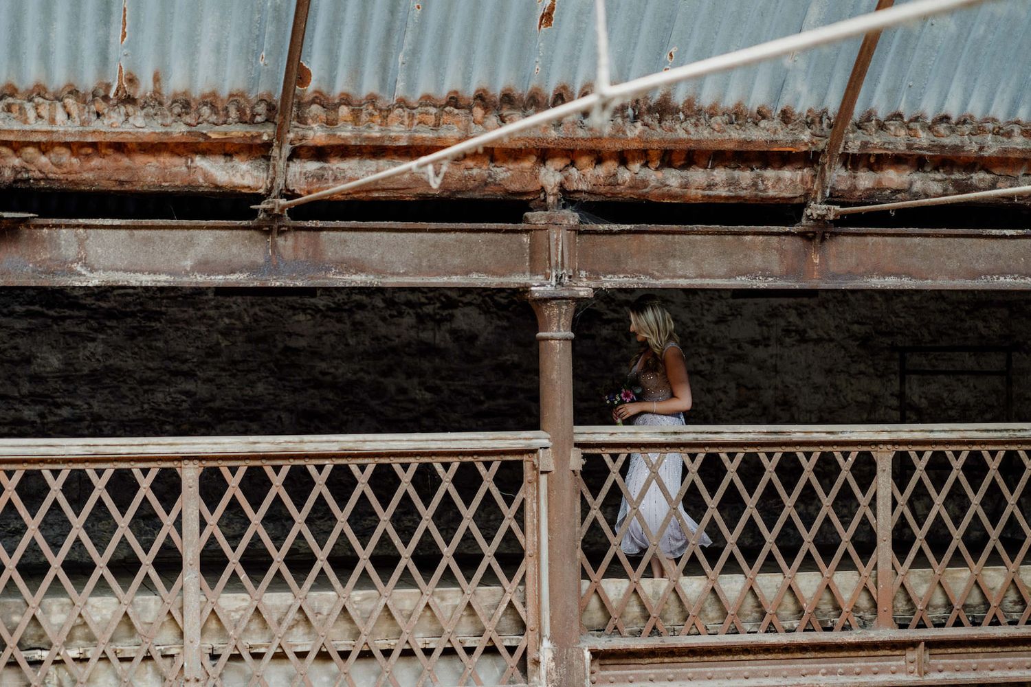 A lone figure stands on a rustic metal walkway with vintage railings.