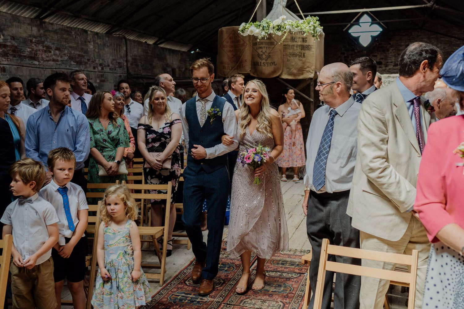 Wedding guests gathered in a rustic barn venue with exposed brick walls.