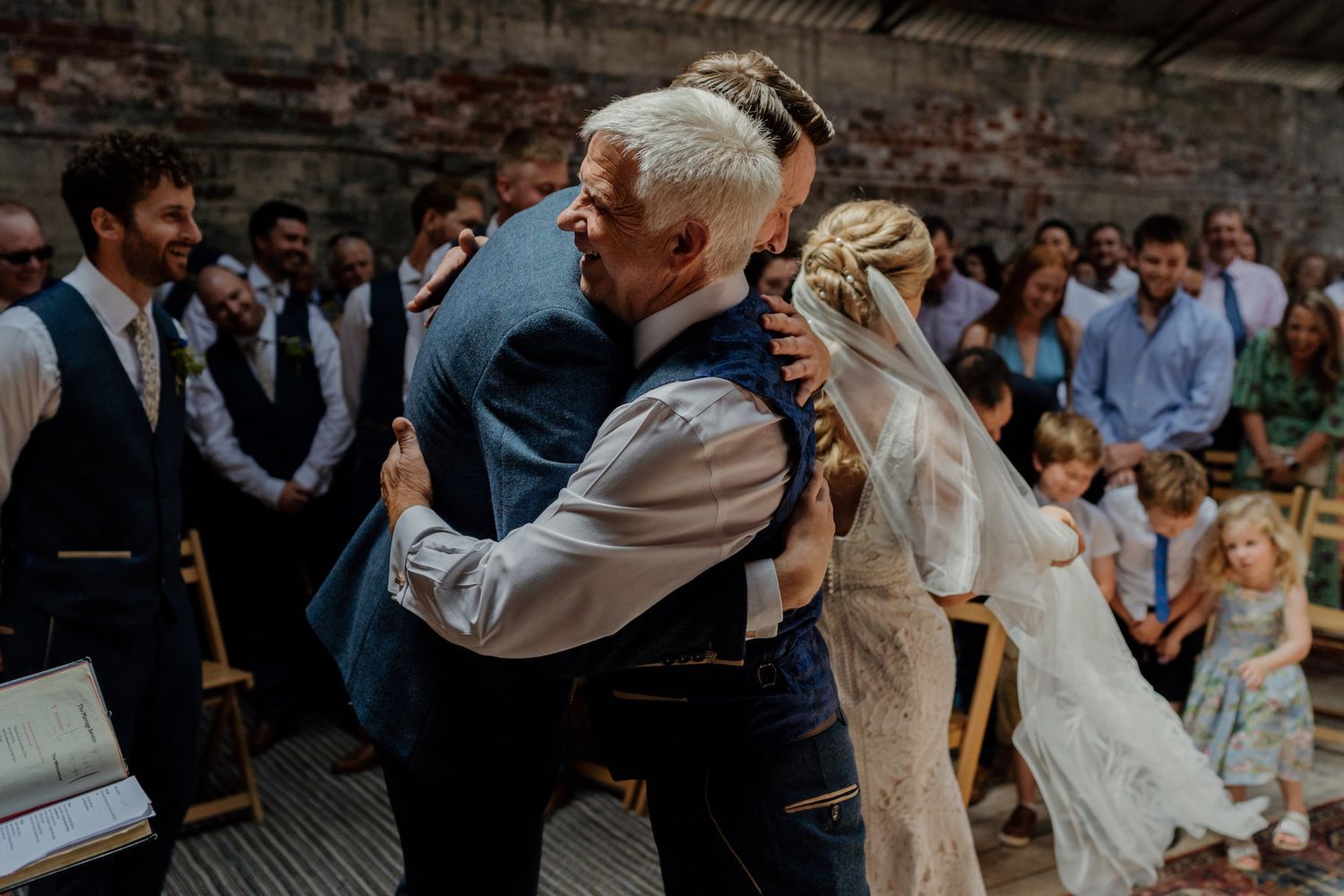 Guests watching an emotional embrace during a wedding celebration in a rustic venue.