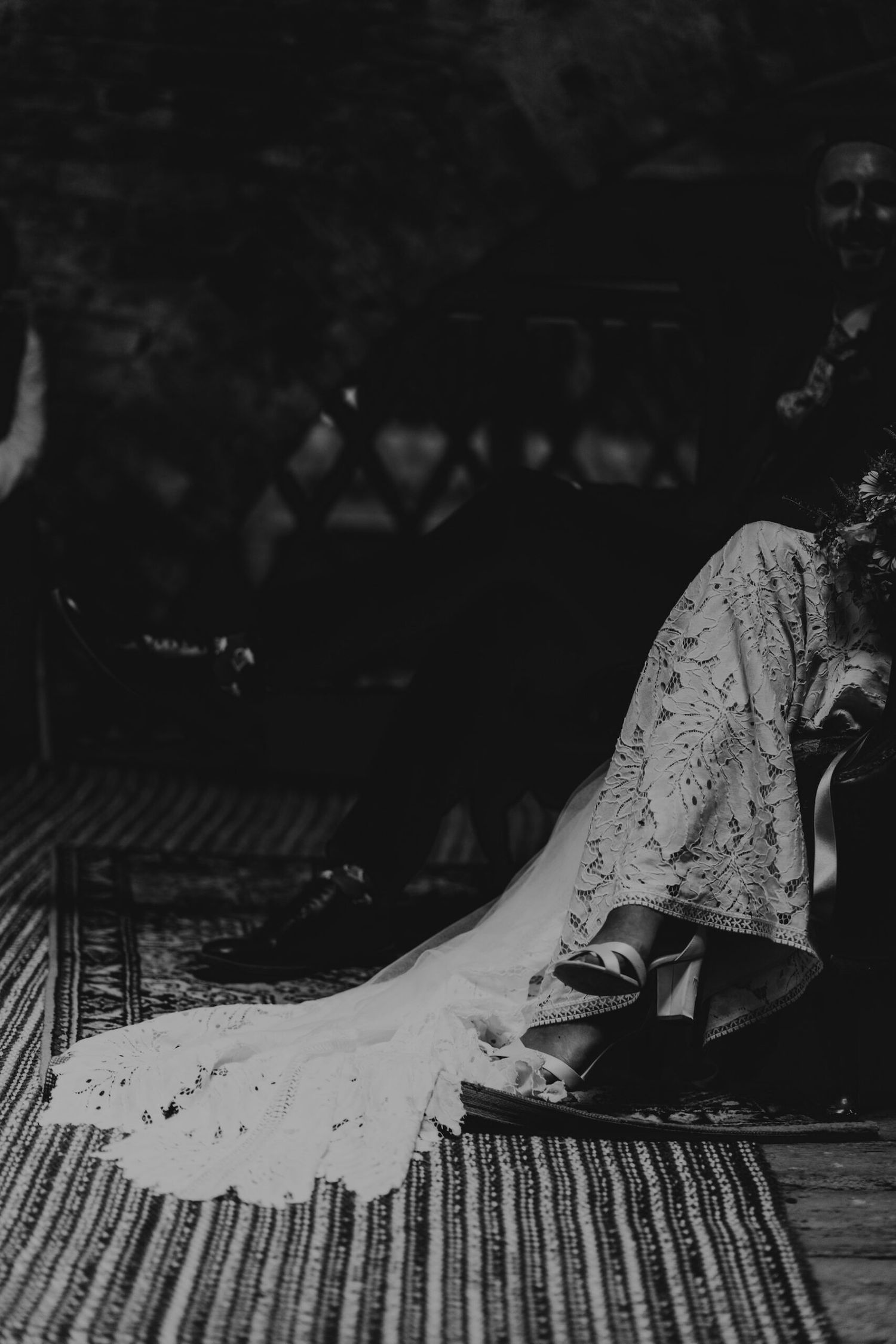 Black and white detail shot of a lace wedding dress trailing on a patterned floor.