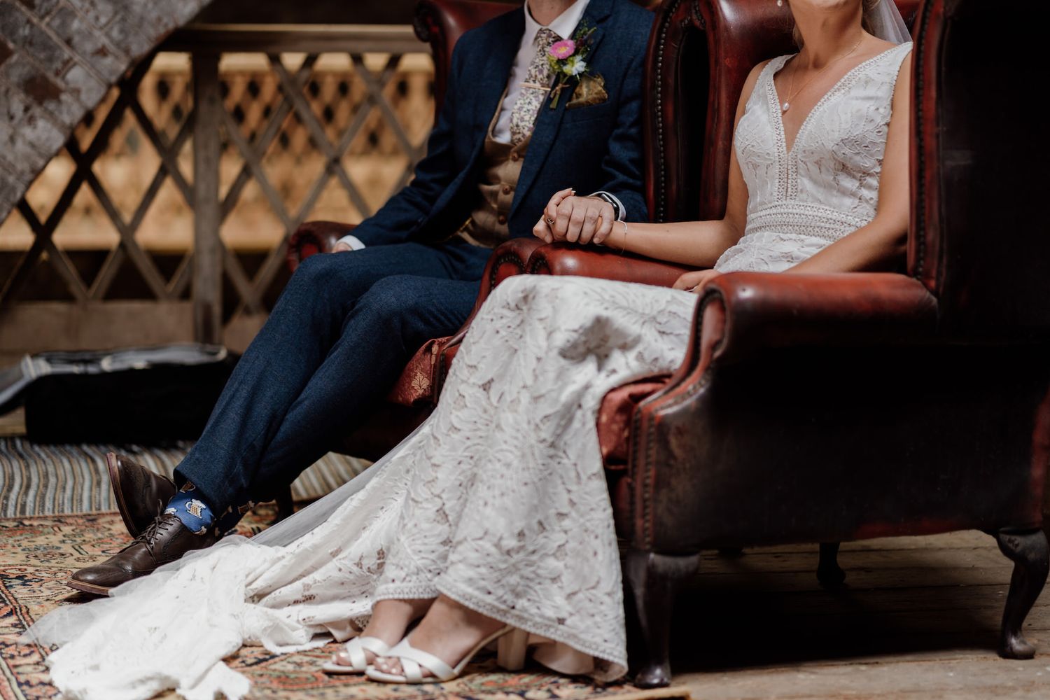 A close-up shot of a wedding couple sitting on a vintage leather couch showing dress details.