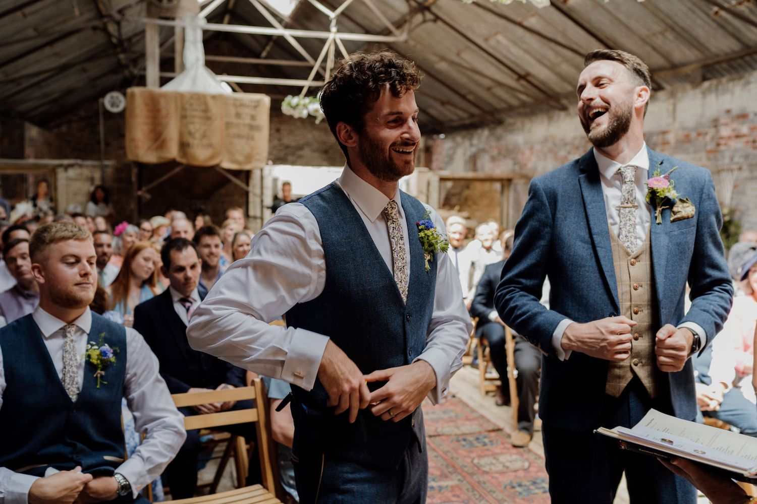 Candid moment of laughter during wedding speeches in a rustic barn venue.