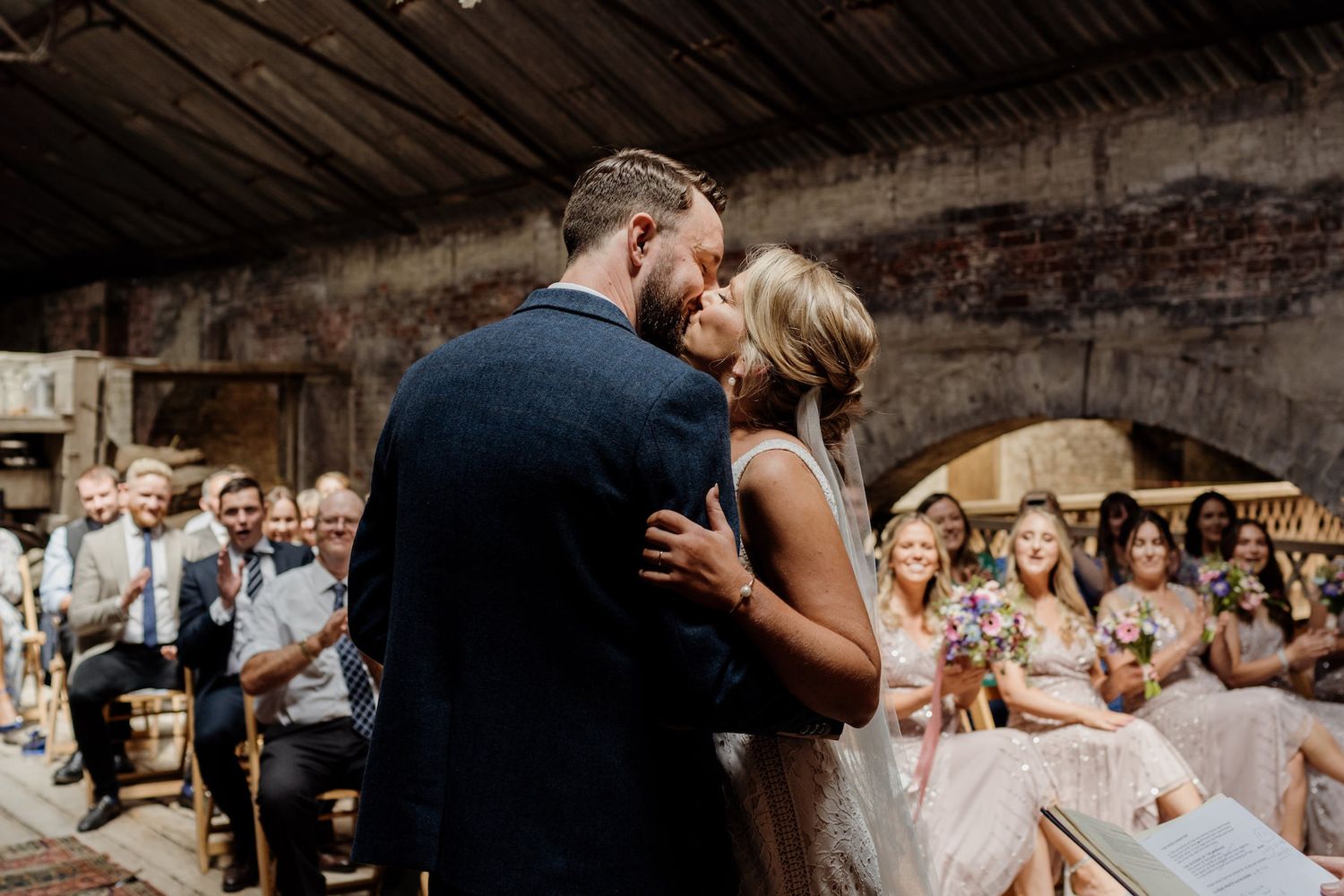 A romantic moment during a rustic barn wedding with guests looking on.