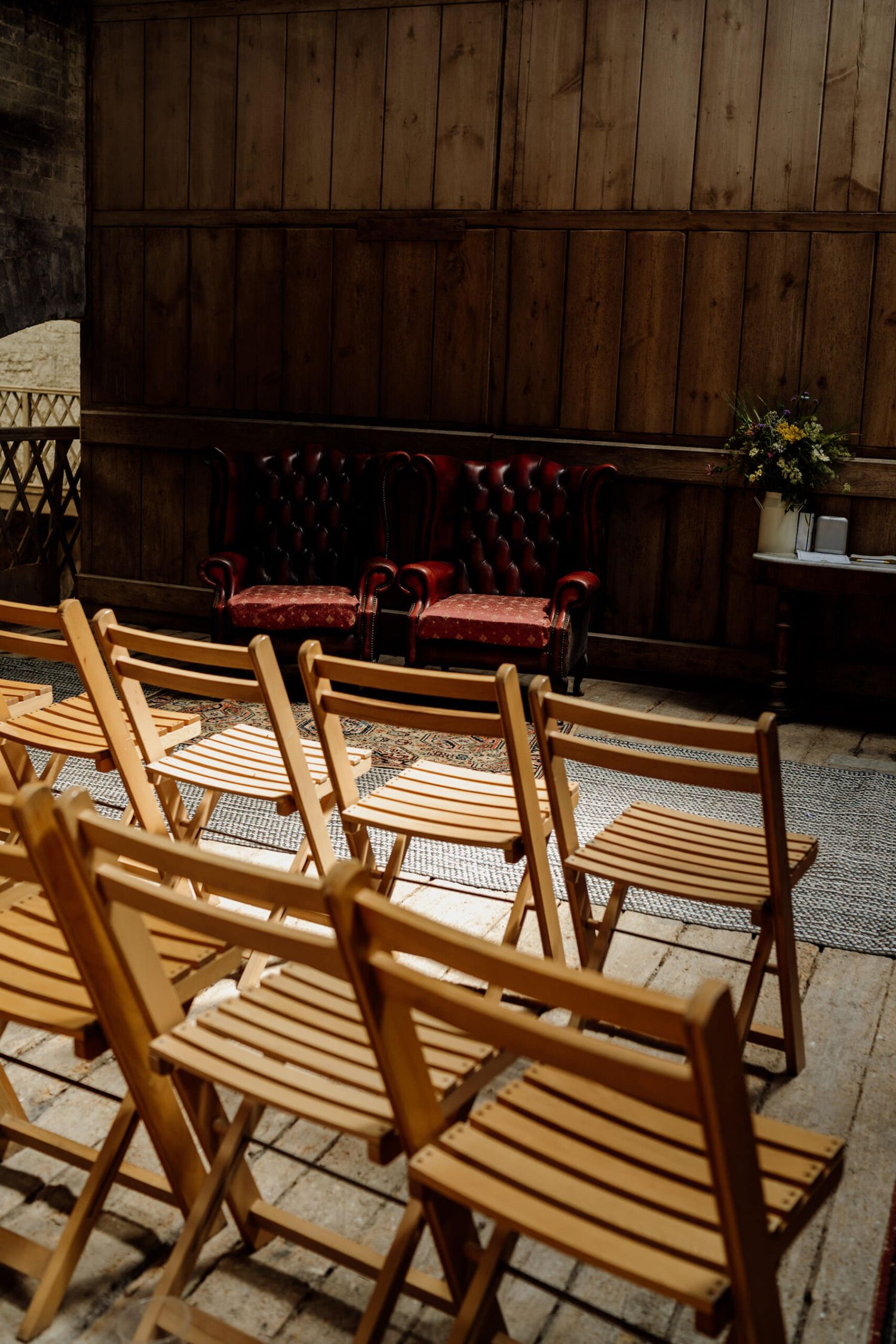 Wooden folding chairs and vintage leather seating arranged for a barn wedding ceremony.