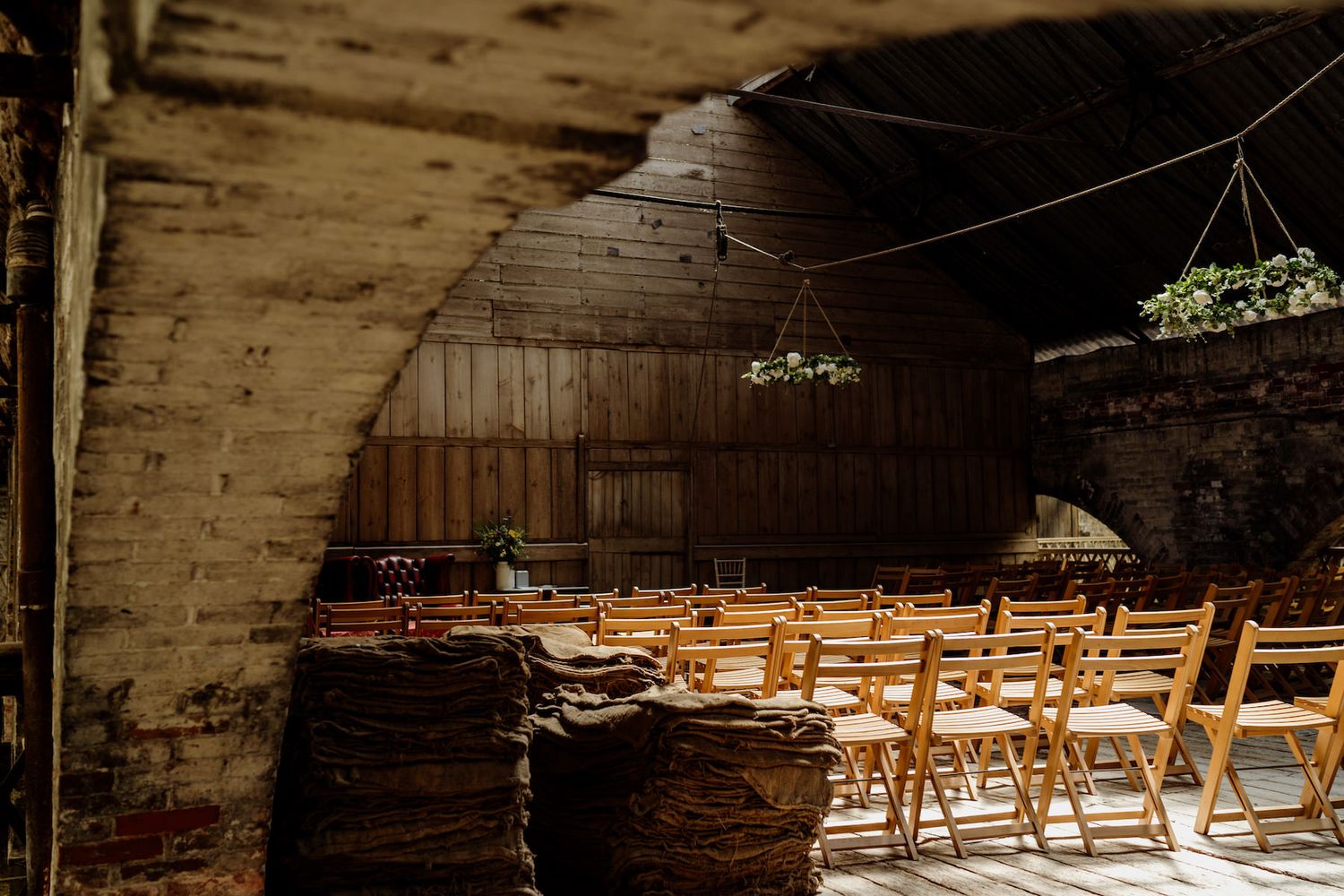 Empty wooden folding chairs set up for a ceremony in a rustic barn venue with hanging decorations.