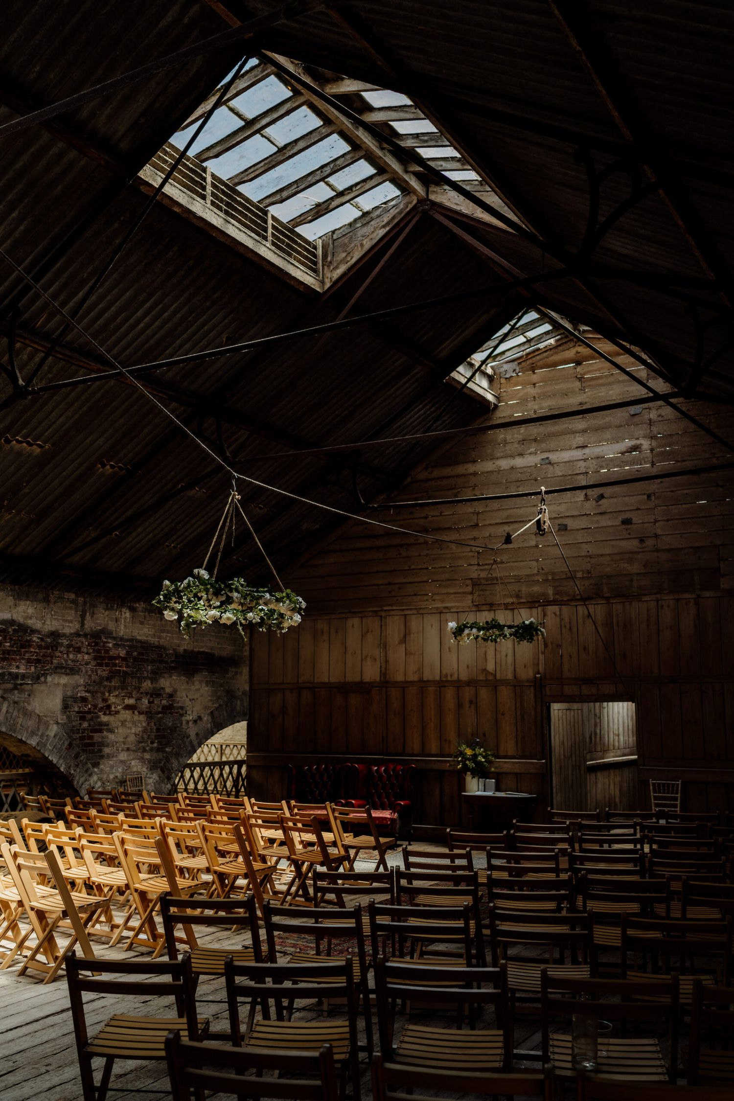 Rustic wooden barn interior set up for wedding ceremony with rows of chairs and skylights overhead.