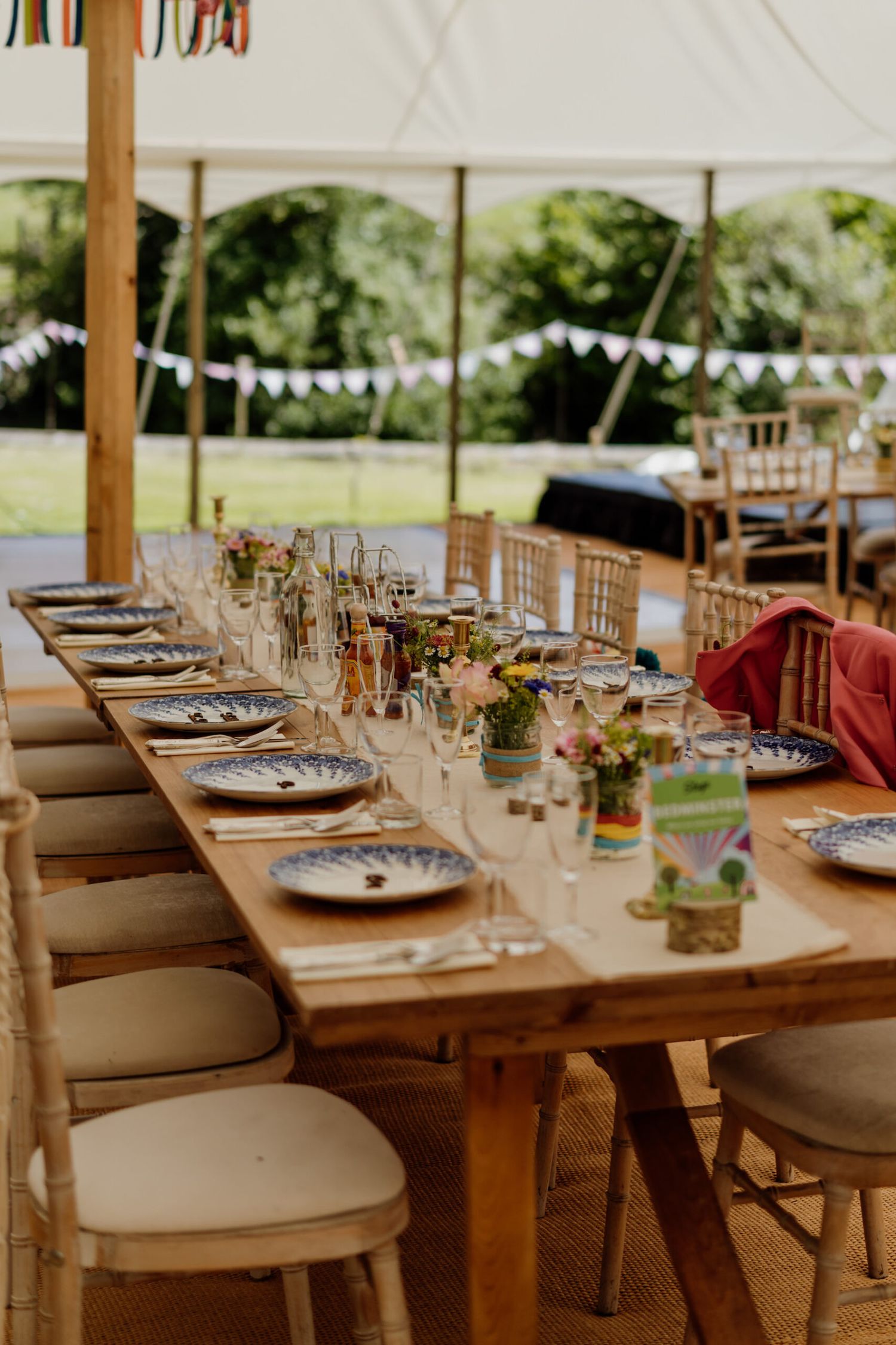 Elegant outdoor wedding reception table settings with wooden tables and white cushioned chairs.