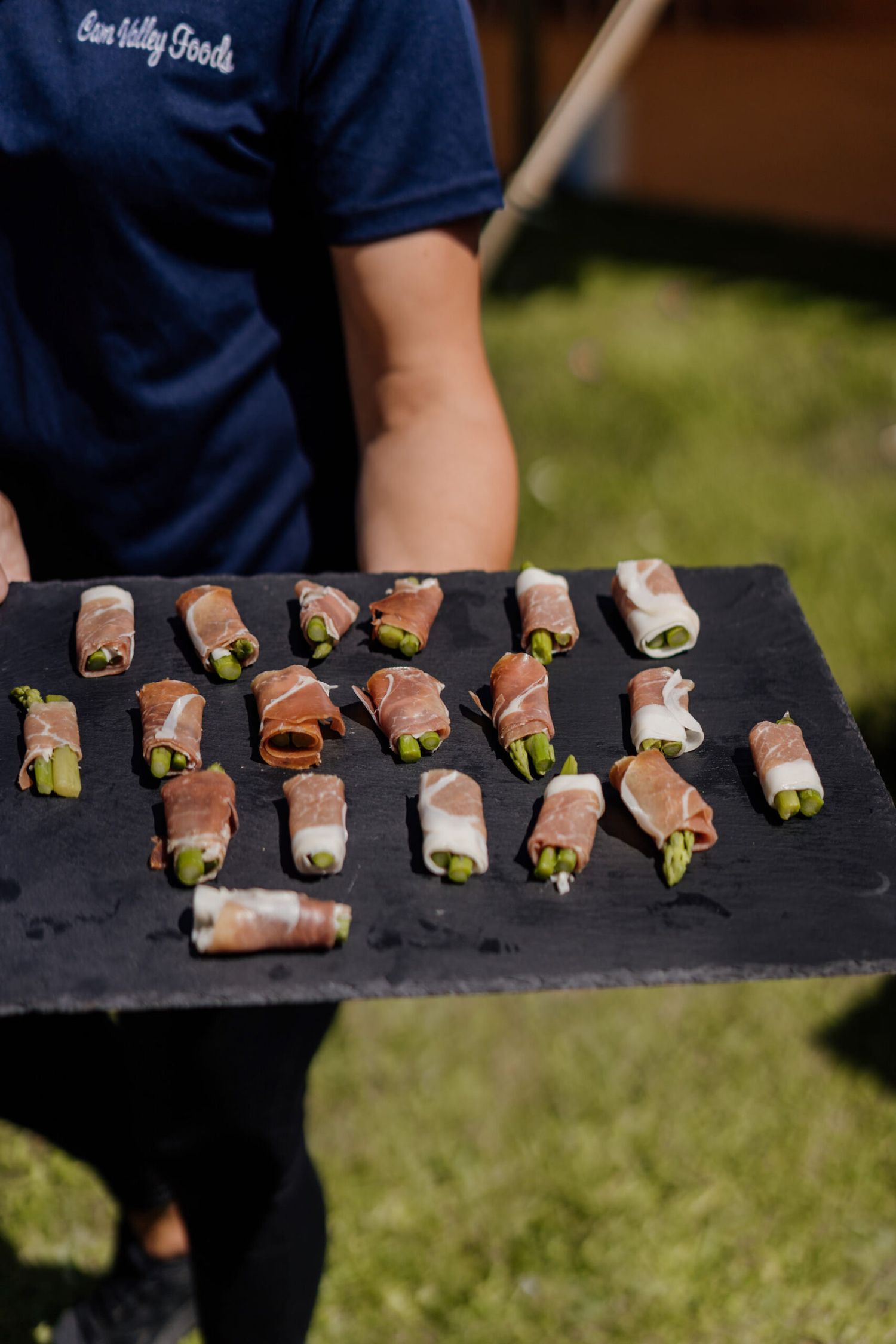 Catering staff presents appetizers on black slate boards at outdoor event.