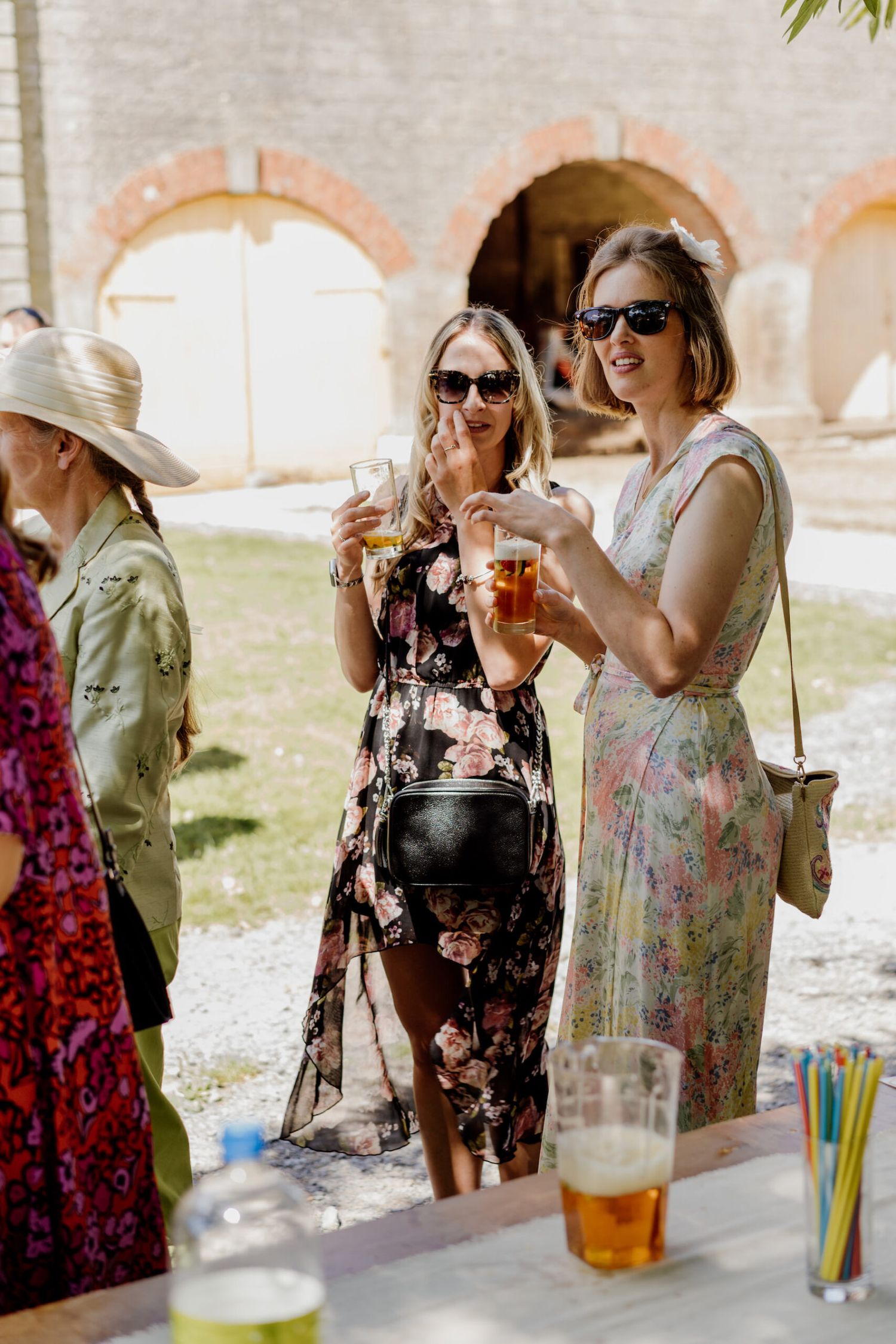 Wedding guests in summer dresses mingling and enjoying drinks at outdoor reception.