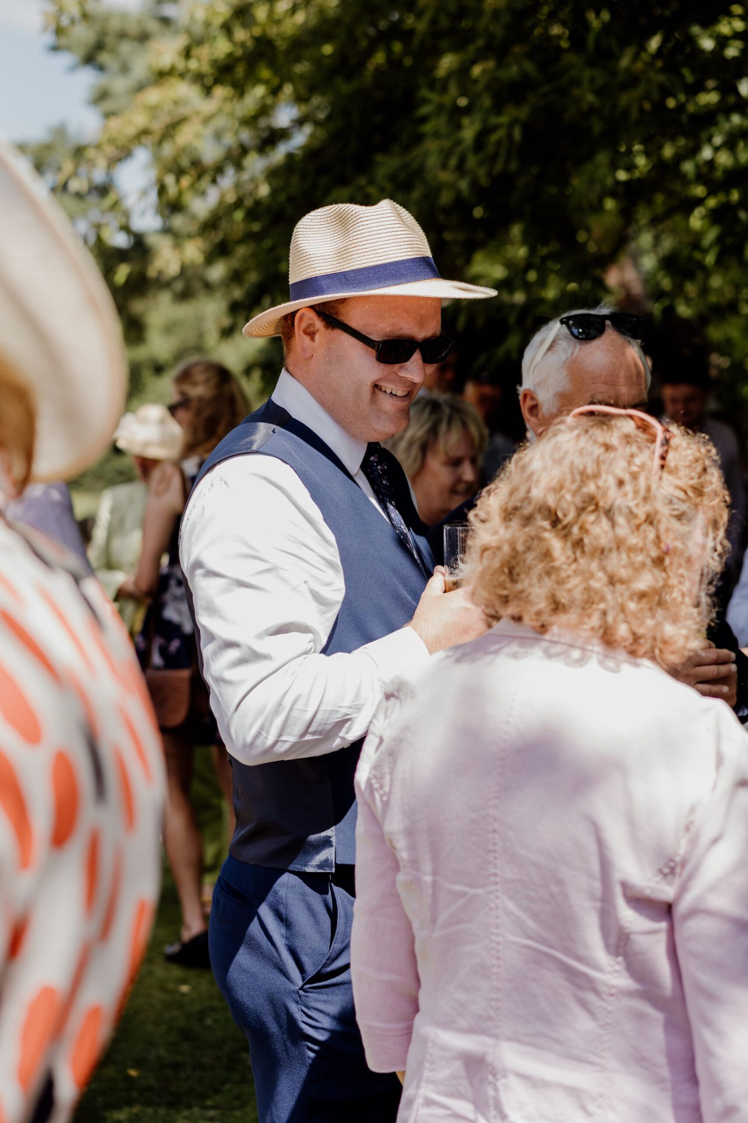 Guests mingling at an outdoor summer garden party wearing hats and sunglasses.