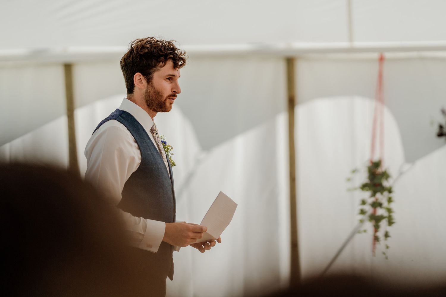 A person in formal attire delivers a speech during an indoor wedding reception.