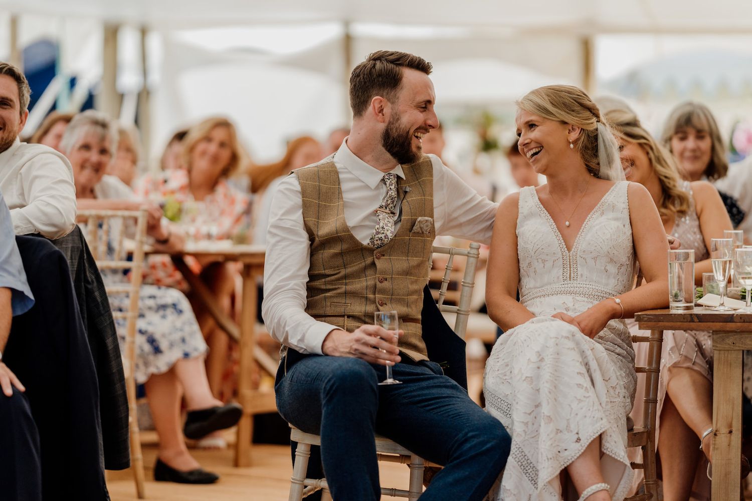 A couple shares a joyful moment during their wedding reception while seated among guests.