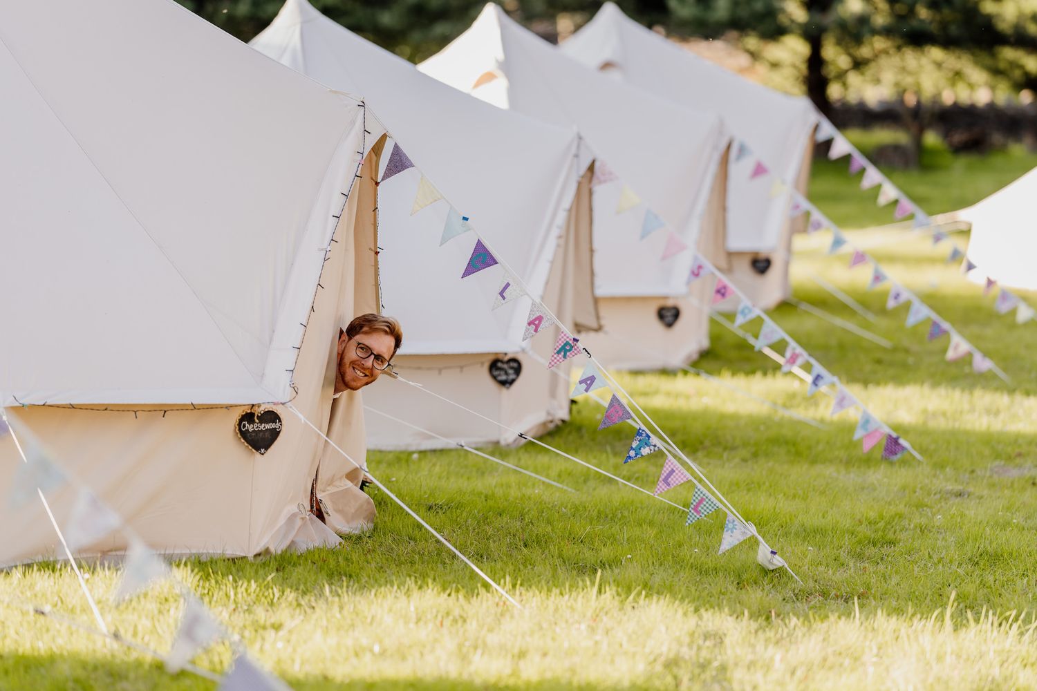 Row of white canvas tents with bunting decorations set up for outdoor wedding celebration.