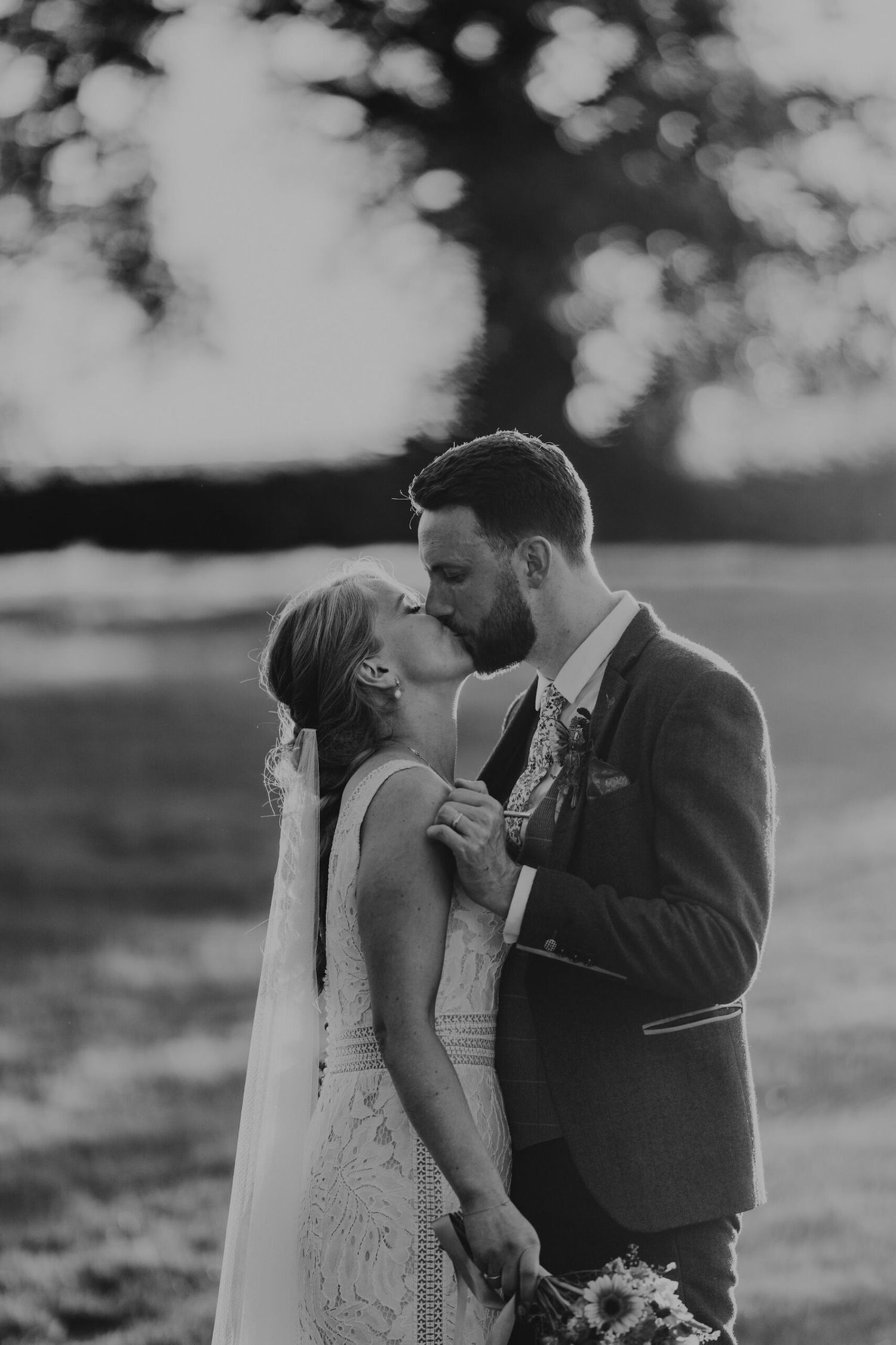 Black and white romantic sunset portrait of newlyweds in field.