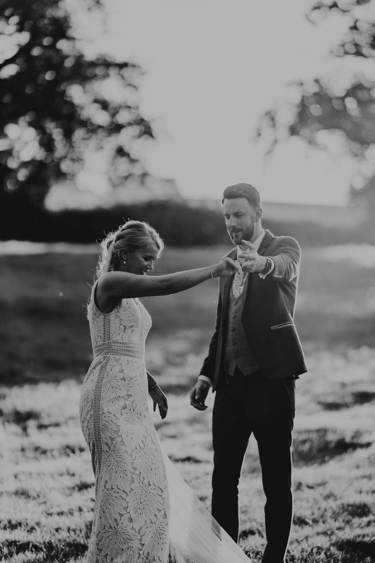 Wedding couple dancing together in a field during golden hour with elegant white lace dress and dark suit.