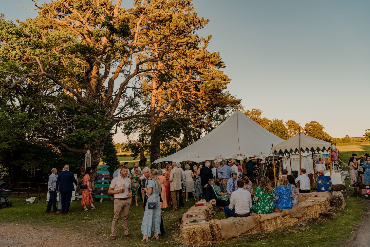 Outdoor wedding reception setup with string lights and tents during sunset.