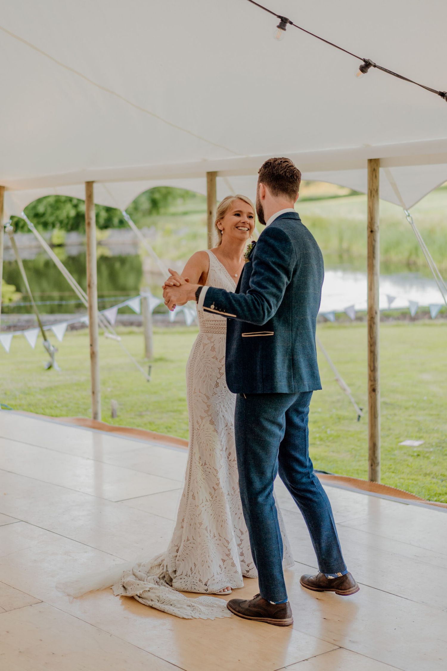 Wedding couple dancing under white tent on wooden floor during reception.