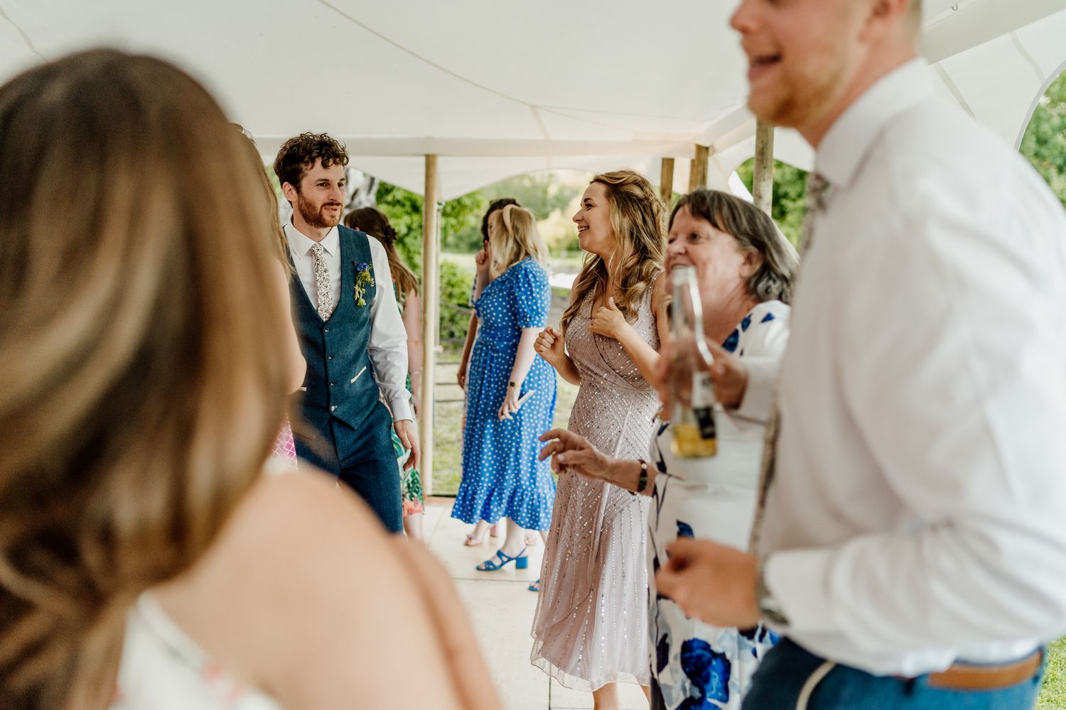 Wedding guests mingling and enjoying refreshments at an outdoor reception under a tent.