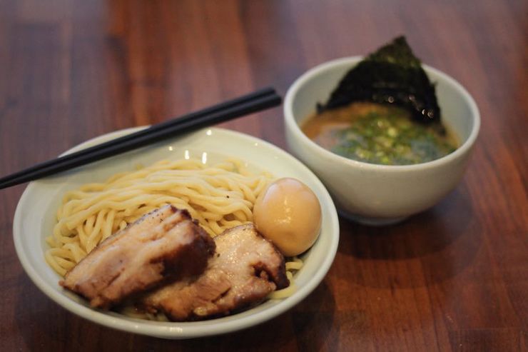 A bowl of ramen noodles with chashu pork and marinated egg served alongside a small bowl of green soup.