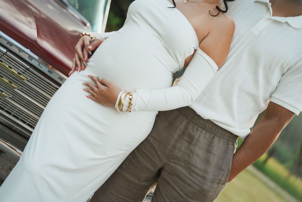 Two people in casual white and beige summer outfits stand close together outdoors.