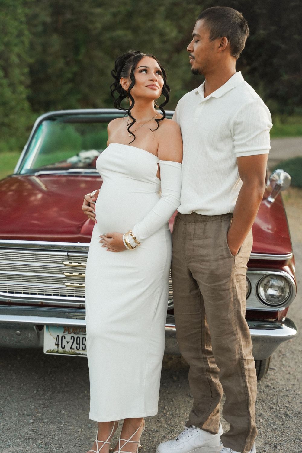 A couple poses affectionately in front of a vintage burgundy car during an outdoor photo session.