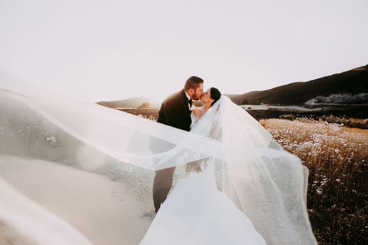 A couple shares intimate moments during their wedding photoshoot in a scenic outdoor meadow at sunset.