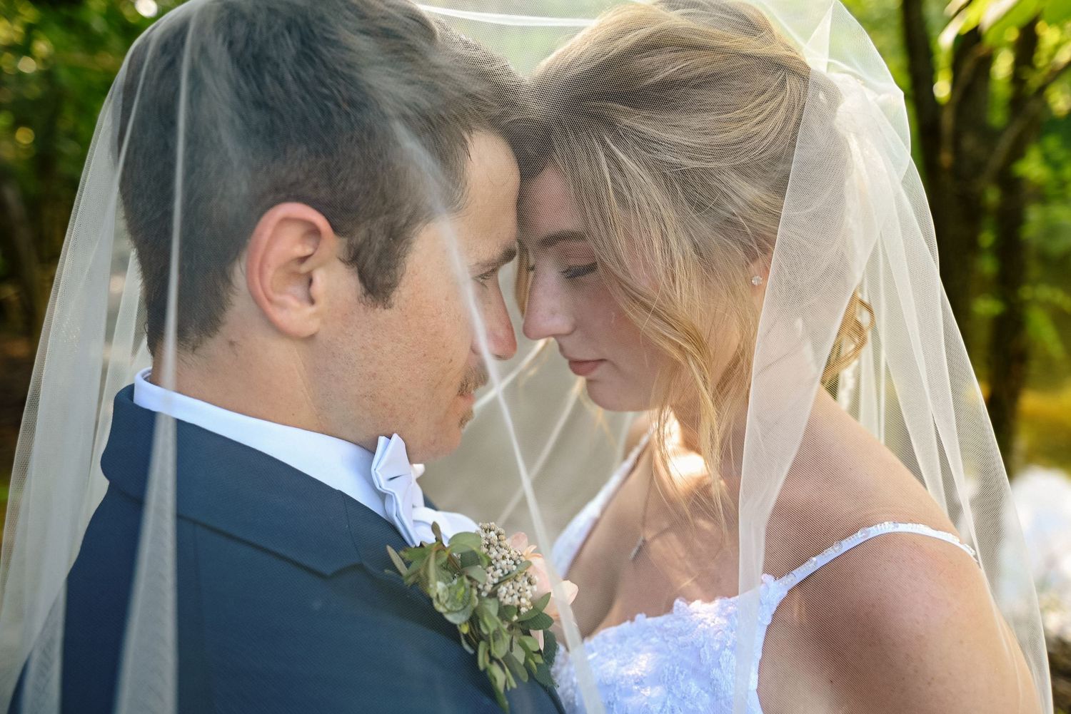 Intimate wedding portraits under green foliage with sunlight streaming through.