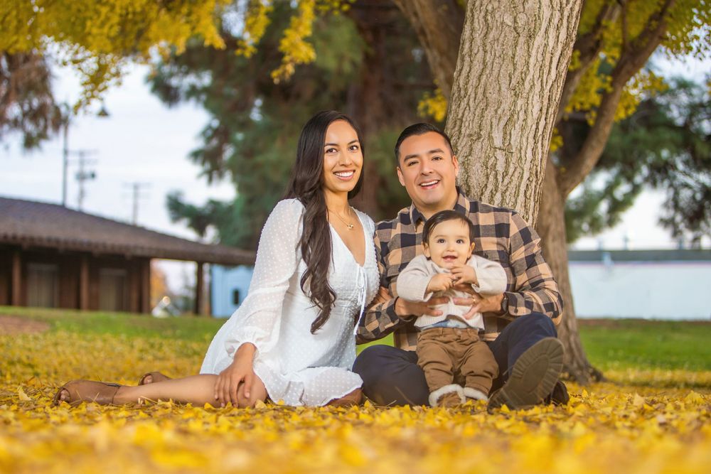 Family enjoying autumn day together sitting on fallen yellow leaves in park setting.