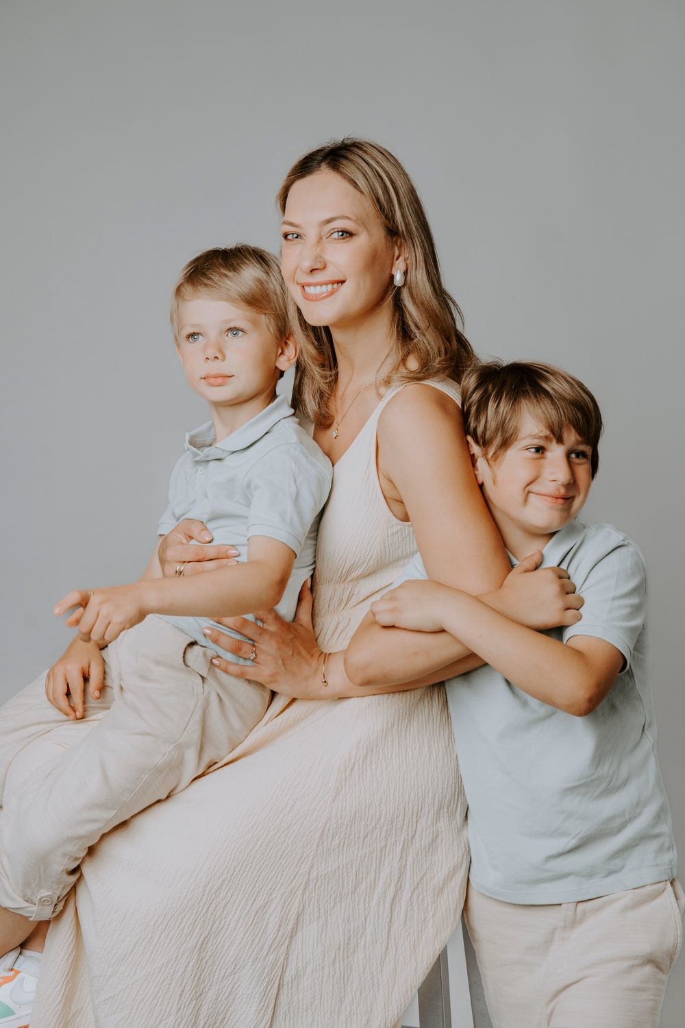 Studio portrait of three people in neutral colored clothing posing together against grey background.