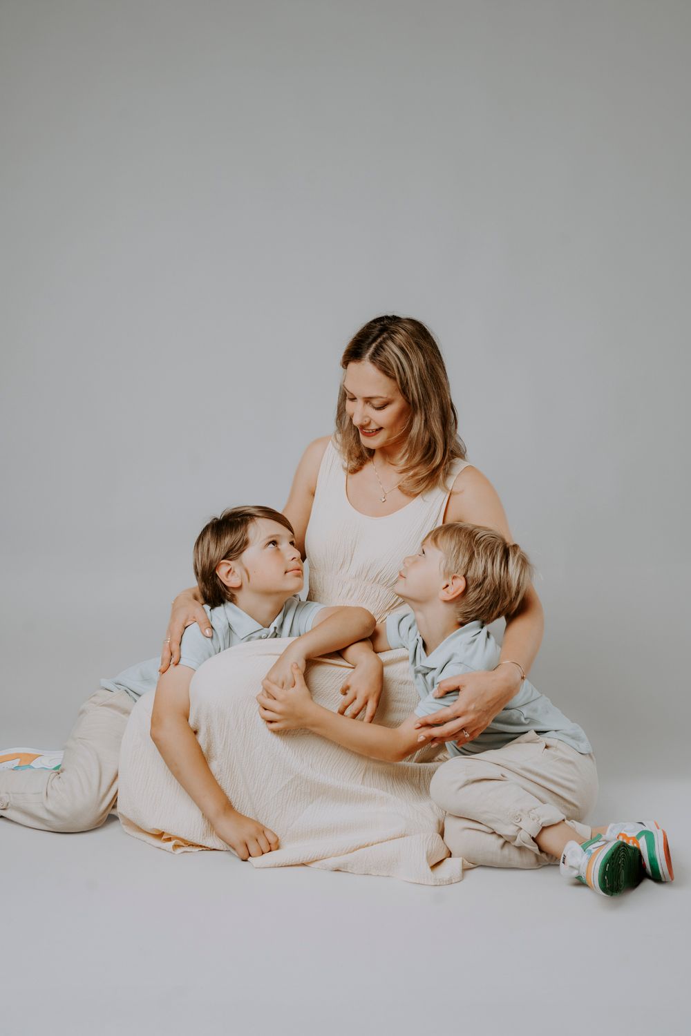 Candid family photo of three people in light colored clothing sitting together on a floor.