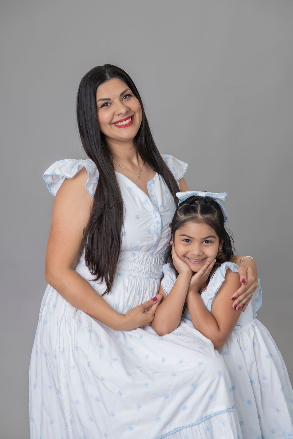 Portrait of two people in white dresses posing together against grey background.