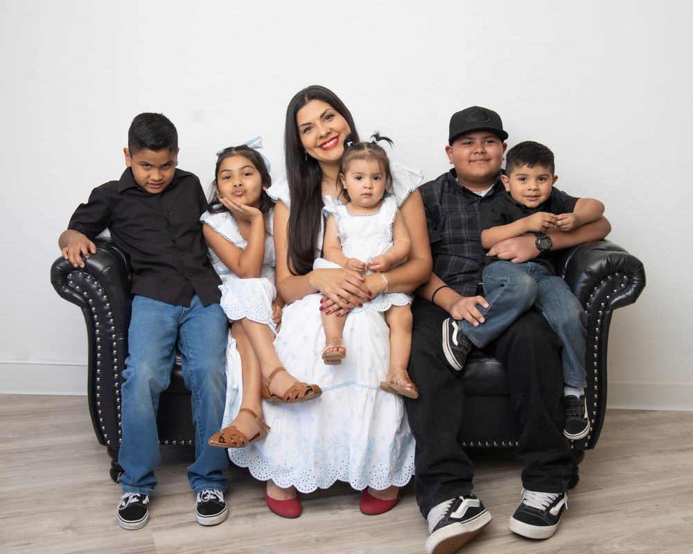 Family portrait of six people dressed in black and white sitting together on a tufted leather sofa.